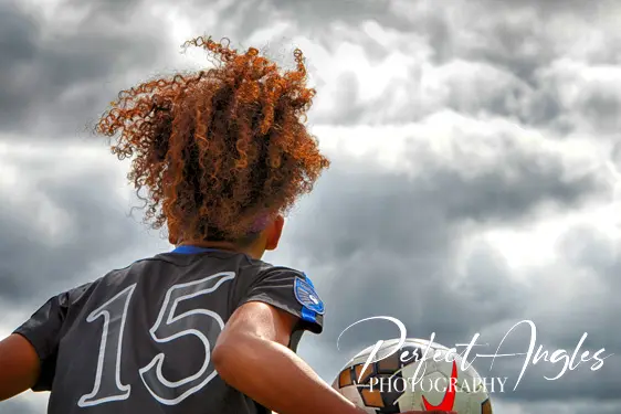 Youth soccer player with curly hair against cloudy sky