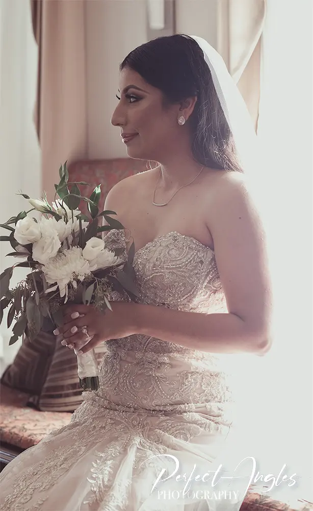 Bride holding a bouquet, looking toward the window light
